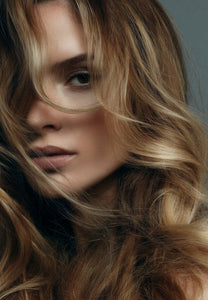 Close-up of a woman with long wavy hair in blended blonde and brown tones, styled after a blow dry