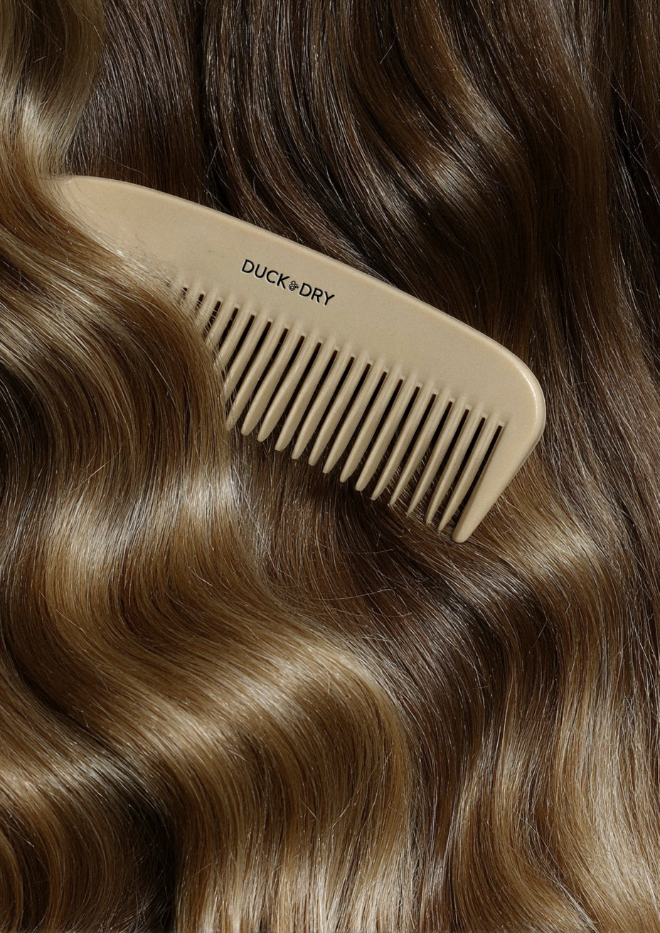 Beige comb with 'Duck & Dry' branding on wavy brown hair