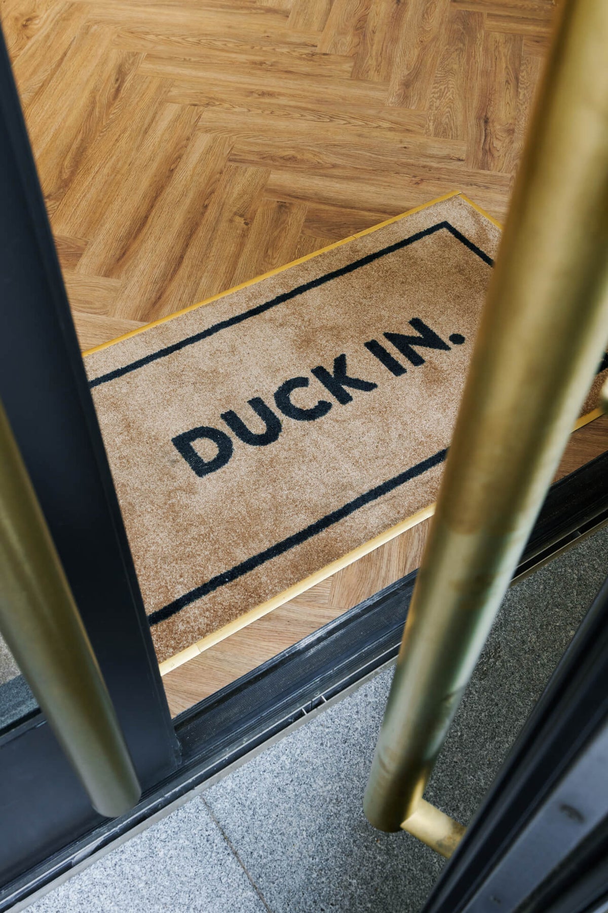 Duck & Dry Mayfair salon doorway with a "Duck In." mat on the herringbone wood floor