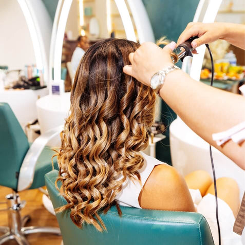 Stylist curling a client's long hair with a wand at a Duck & Dry blow dry lesson