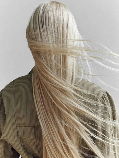 Woman with long, flowing blonde hair blow dry on a plain background