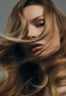 Front profile of a woman with wavy blonde and brown hair, highlighting a bouncy blow dry style