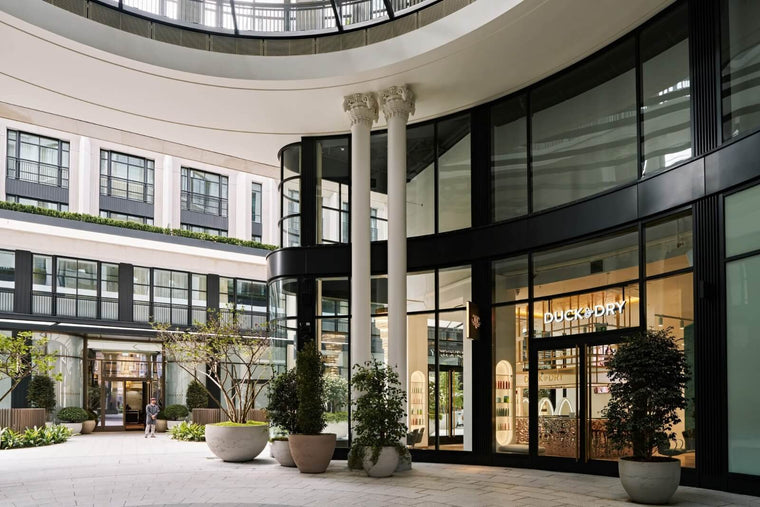 Exterior of a Duck & Dry London salon with warm interior lighting and a curved glass facade