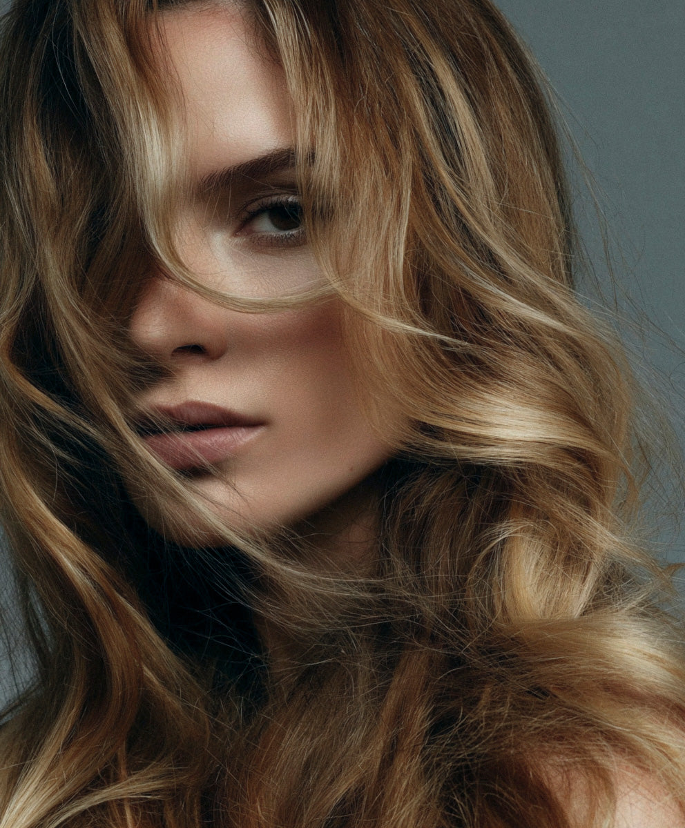 Close-up of a person with wavy blonde hair against a neutral background