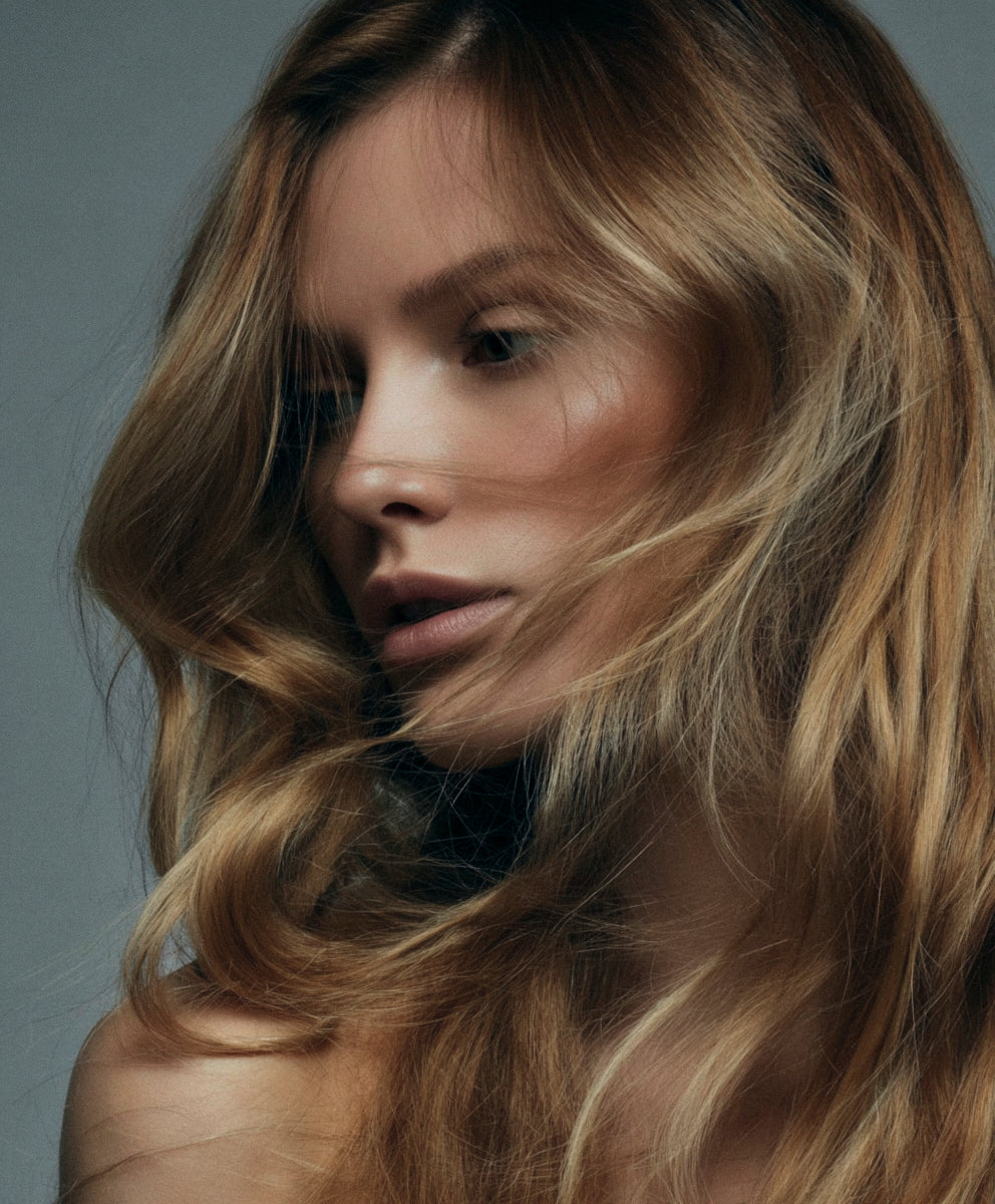Close-up of a person with wavy blonde hair against a gray background