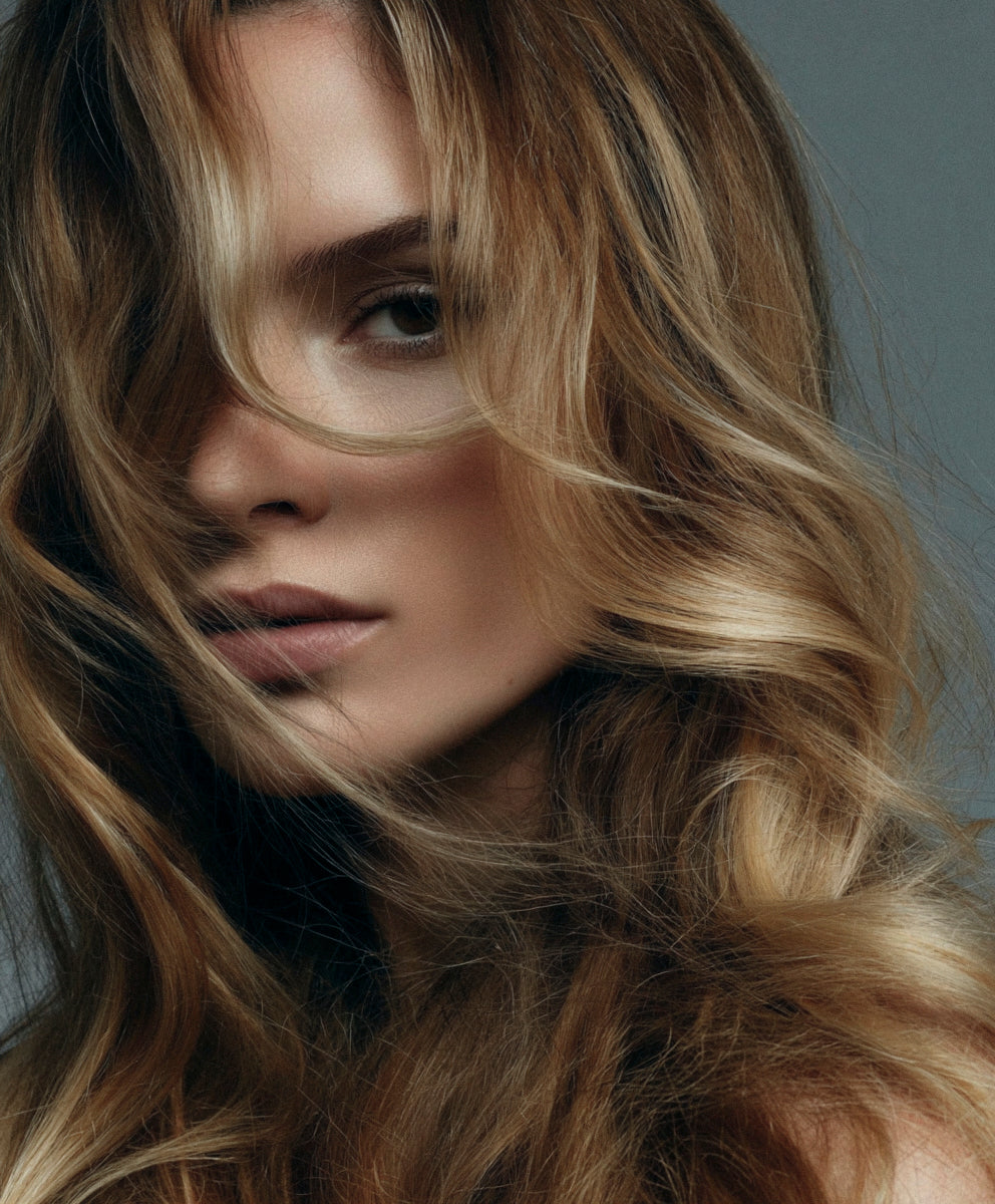 Close-up of a person with wavy blonde hair against a neutral background
