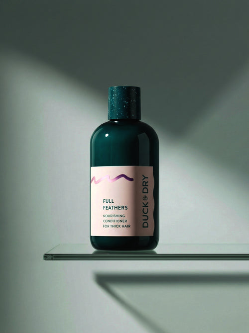 Bottle of Duck & Dry Full Feathers conditioner on a glass shelf with a gray background
