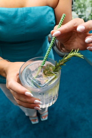 Woman holding a cocktail with a Duck & Dry branded ice cube, garnished with rosemary and a paper straw