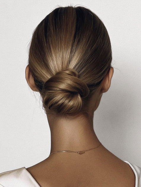 Woman with chelsea bun updo as seen from the back on a plain background