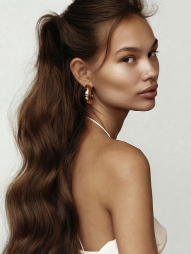 Woman with long wavy hair styled in a high ponytail on a plain background