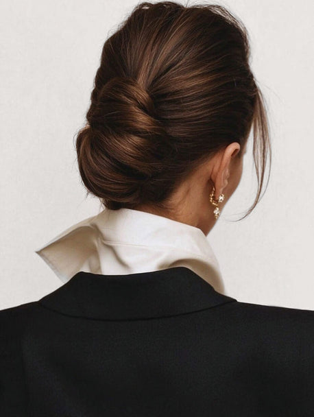 Woman wearing a black blazer and white shirt with a stylish hair bun updo on a plain background